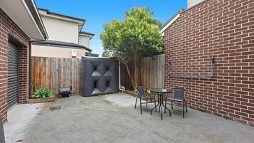 A backyard with a brick wall, a wooden fence, a tree, and outdoor furniture.