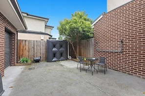 A backyard with a brick wall, a wooden fence, a tree, and outdoor furniture.
