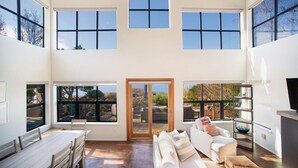 A spacious interior with a high ceiling, large windows, a sliding glass door, a white sofa, a dining table, and a TV. - Langley Waterfront Oasis with Hot Tub (Langley)