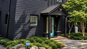 A modern two-story house with a dark exterior, a blue door, and a stone chimney. - Langley Waterfront Oasis with Hot Tub (Langley)