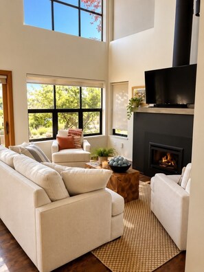 A modern living room with a fireplace, large windows, and a flat-screen TV. - Langley Waterfront Oasis with Hot Tub (Langley)