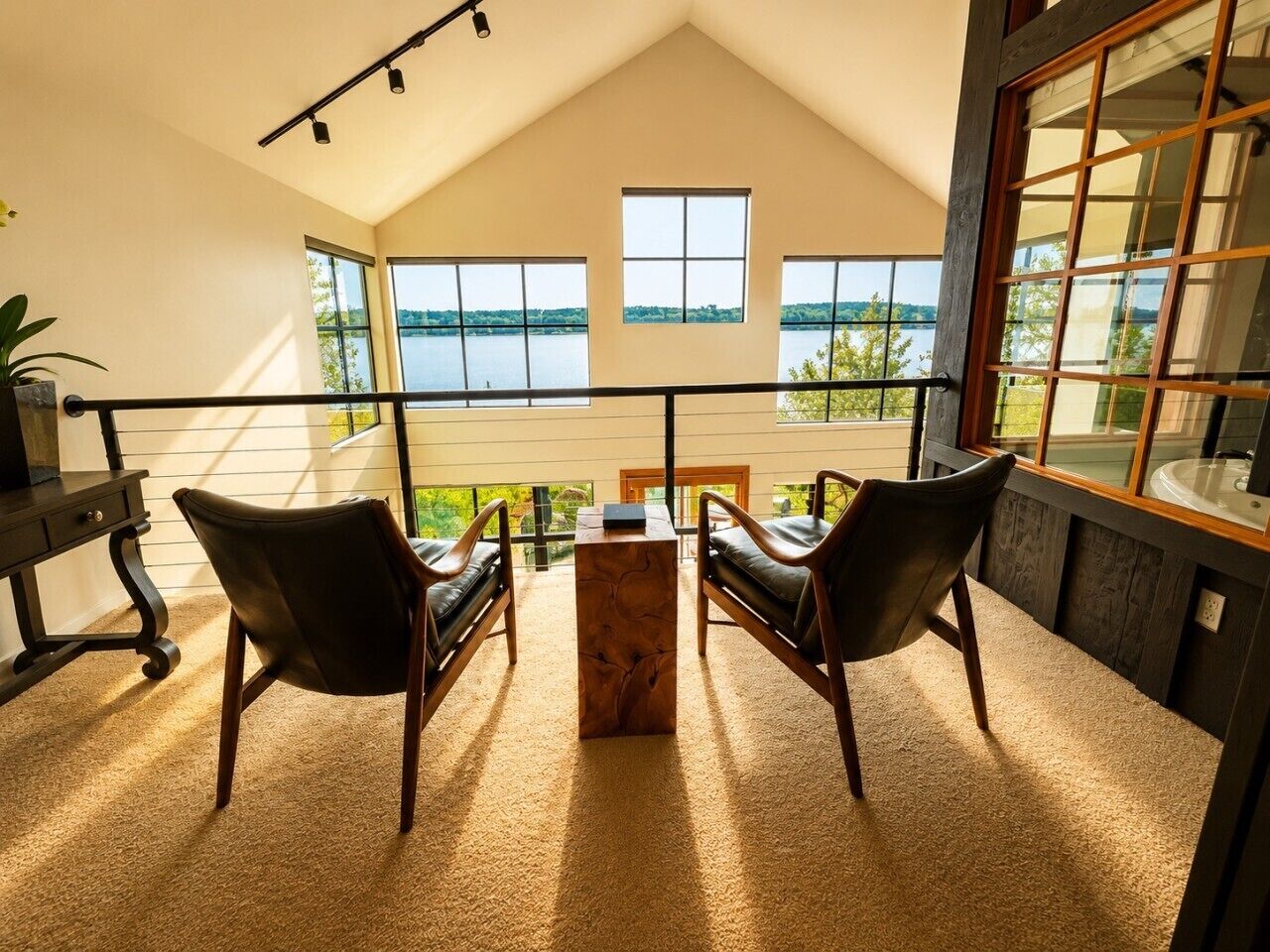 A room with a view of a lake, a wooden coffee table, two leather chairs, and a large window.