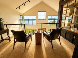 A room with a view of a lake, a wooden coffee table, two leather chairs, and a large window. - Langley Waterfront Oasis with Hot Tub (Langley)