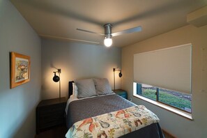 A bedroom with a bed, a ceiling fan, two bedside lamps, a window with blinds, and a framed picture on the wall.