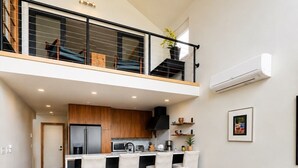 A modern kitchen with a central island, a dining area with a wooden table and chairs, and a staircase leading to an upper level. - Langley Waterfront Oasis with Hot Tub (Langley)