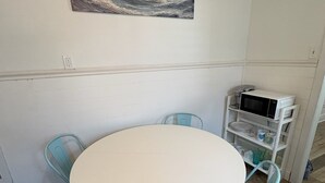 En matplats med ett runt bord, fyra stolar, en mikrovågsugn och en hylla med tallrikar.