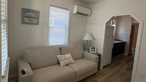 Ett vardagsrum med en beige soffa, en lampa, en tavla och en luftkonditioneringsanläggning på väggen.