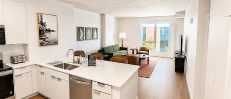 Una cocina moderna con una isla central, una zona de comedor con sofá y sillones, y un amplio ventanal que ofrece luz natural.
