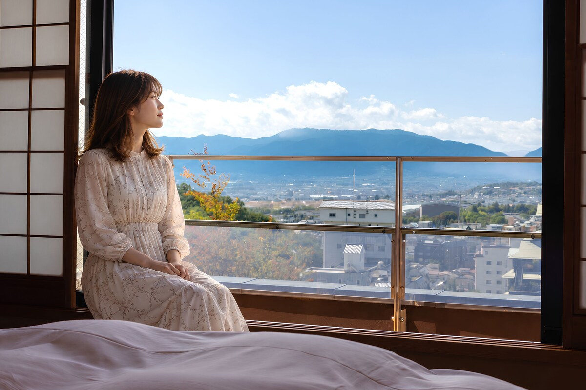 A room with a large window offering a view of a cityscape and mountains.