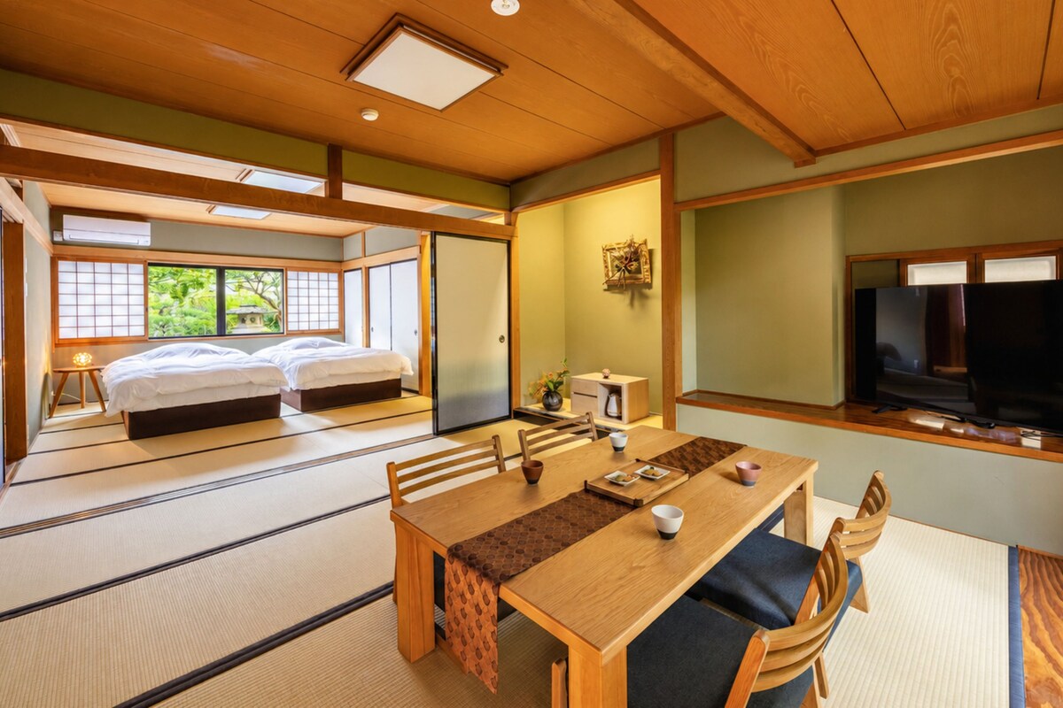 A traditional Japanese-style room with tatami flooring, a low table with cushions, a bed with futon, and a television.