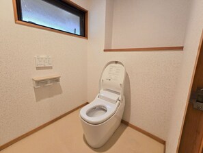 A small, private bathroom with a toilet, a window, and a wall-mounted control panel. - SANEIKAKU (Matsumoto)