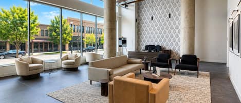 A spacious lobby with a modern design, featuring a seating area with sofas and armchairs, a patterned wall, and large windows offering a view of the street.