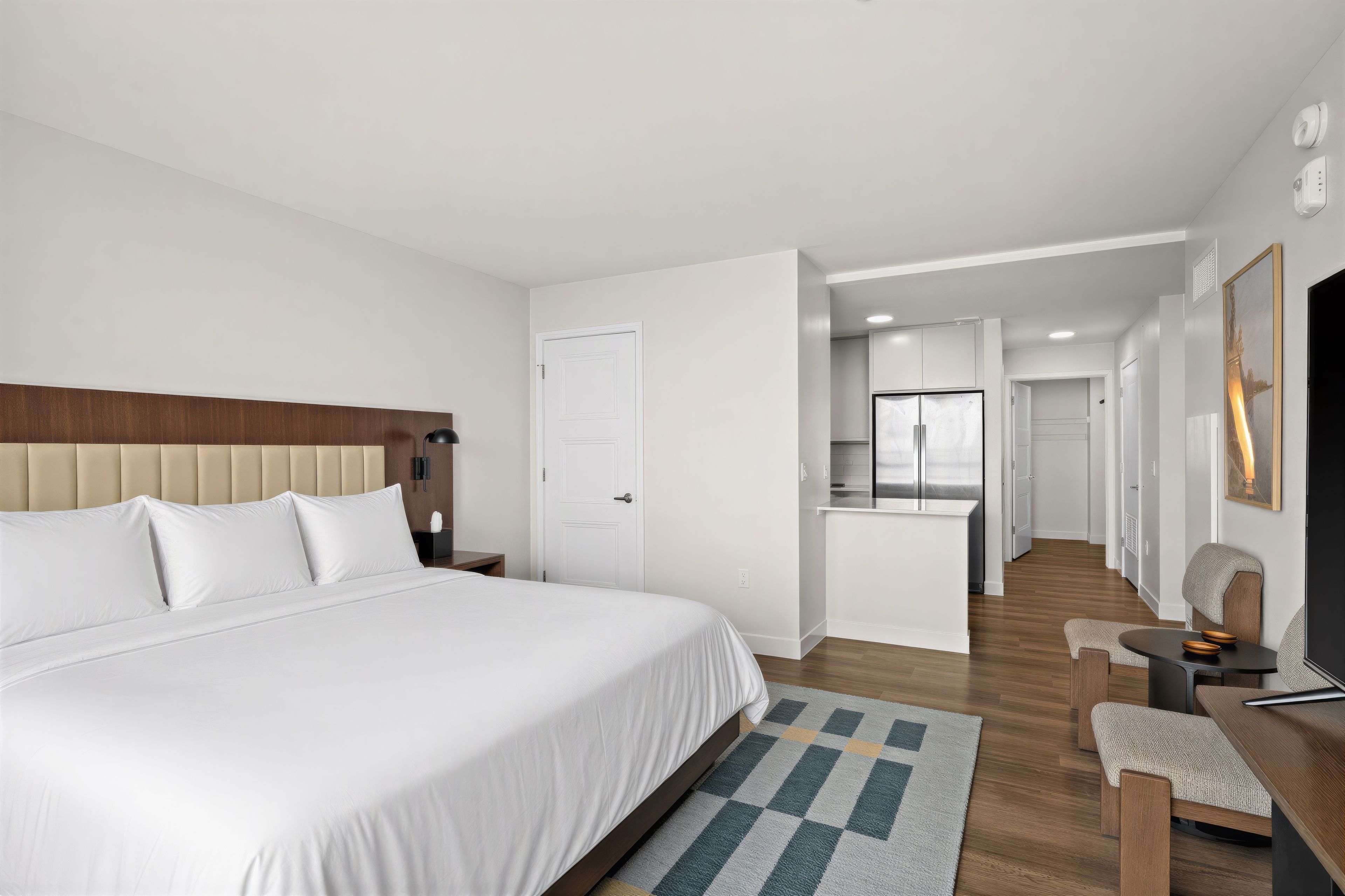 Habitación de hotel con una cama grande, un escritorio, una silla, una mesita, un televisor y una puerta que da a un baño.