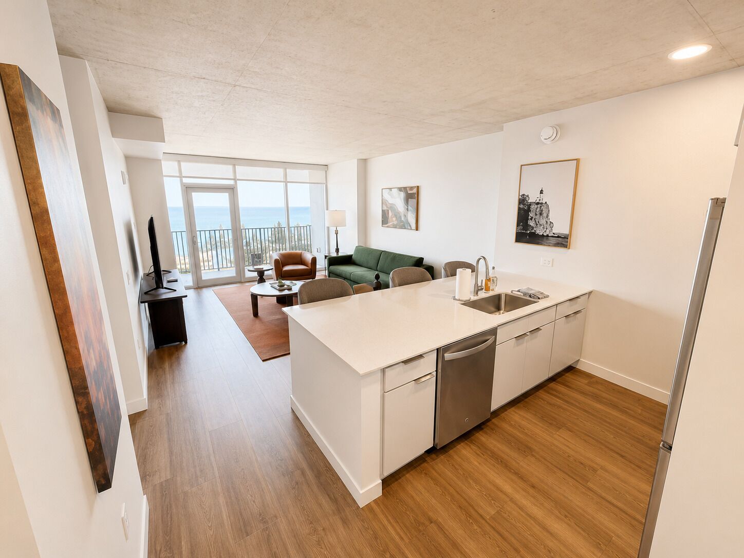Cozinha moderna com máquina de lavar louça, área de jantar com mesa e cadeiras, sofá verde e varanda com vista.