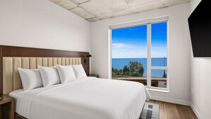 A bedroom with a large bed, a headboard, a nightstand, a window with a view of the sea, and a ceiling with a textured finish. - One Bedroom King bedded room with direct views of Lake Superior (Duluth)