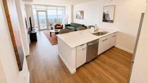 A modern kitchen with a dishwasher, a dining area with a table and chairs, a green sofa, and a balcony with a view. - One Bedroom King bedded room with direct views of Lake Superior (Duluth)