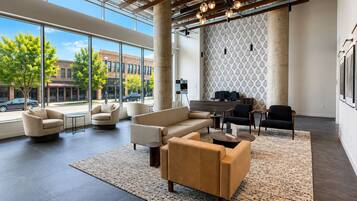 A spacious lobby with a modern design, featuring a seating area with sofas and armchairs, a patterned wall, and large windows offering a view of the street.