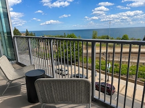 A balcony with wicker furniture, a small table, and a view of the sea and railway tracks. - Large Corner 2 Bedroom/2 Bath Unit with Floor to Ceiling Lake Superior Views (Duluth)