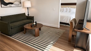 Ein Hotelzimmer mit einer Couch, einem runden Couchtisch, einer Lampe, einem Bett und einem Schreibtisch mit einem Computer.