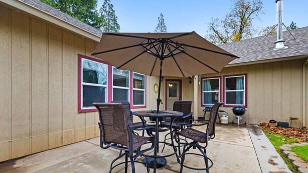 An outdoor patio with a table and chairs, a large umbrella, and a barbecue grill. - Chalet di Montagna ~ Spacious house in the pines (Mi-Wuk Village)