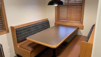 A corner seating area with a bench and a table, wooden blinds, and a pendant light.