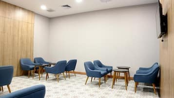 A room with blue chairs arranged around a central table, a patterned carpet, and a wooden panel wall.