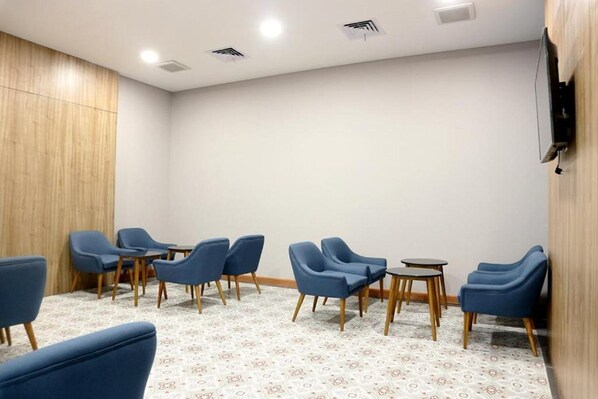 A room with blue chairs arranged around a central table, a patterned carpet, and a wooden panel wall. - Cordia Banjarmasin (Banjarbaru)