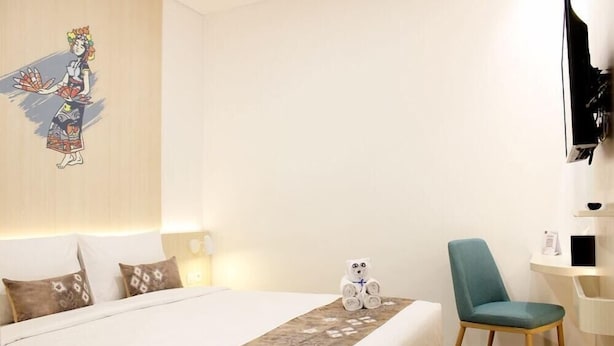 Een hotelkamer met een bed, kussens, een stoel, een tafeltje, een televisie en een decoratie aan de muur.