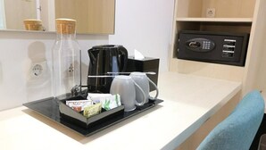 Hotelkamer met koffiehoekje, een zwarte koffiezetapparaat, een glazen fles en een zwarte stroomkast op het aanrecht.