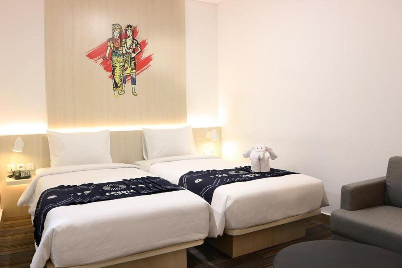 A hotel room with two beds, a sofa, a teddy bear, and a wall art piece.
