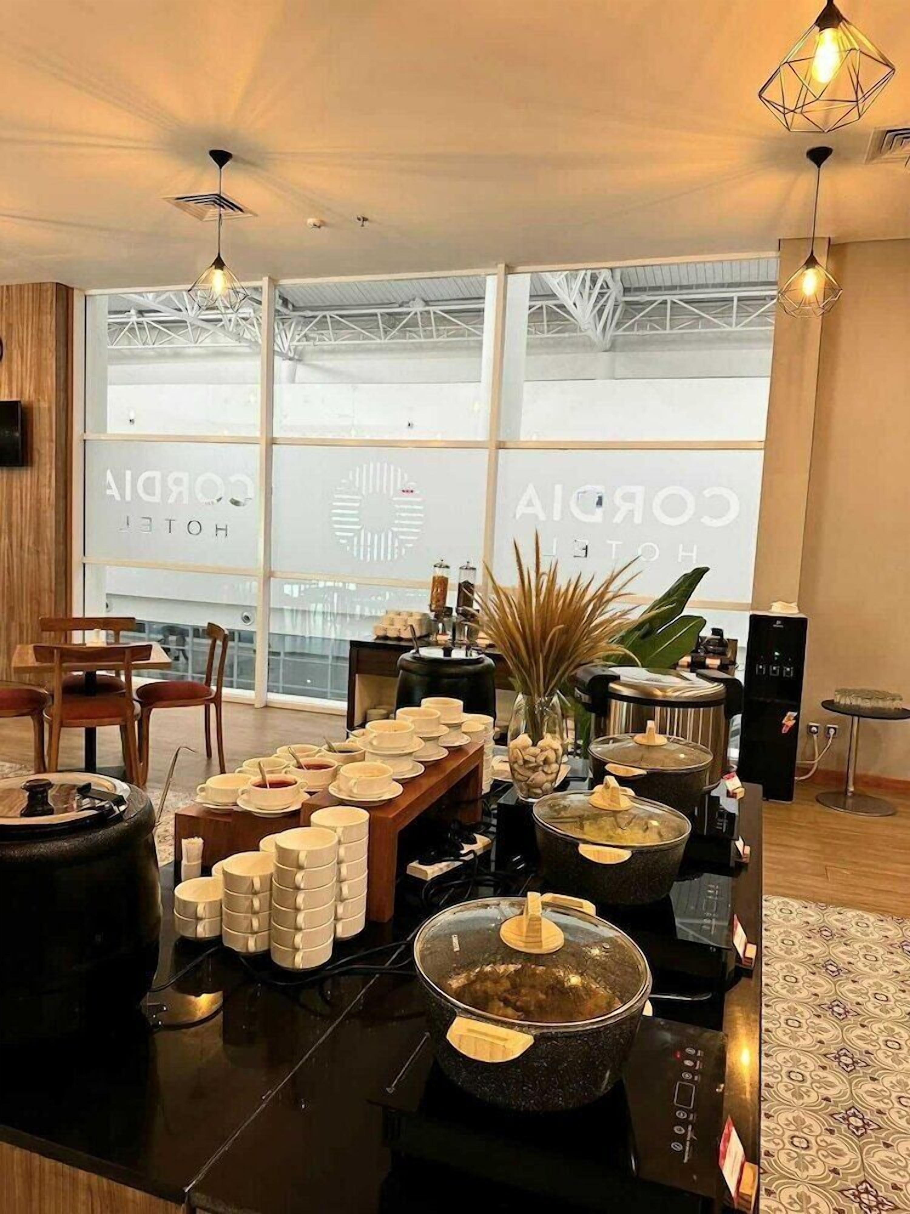 A hotel room with a large window, a dining table set with plates and glasses, and a kitchen area with pots and a stove.