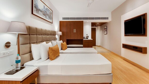 A modern hotel room with a large bed, a desk with a lamp, a television, and a ceiling fan.