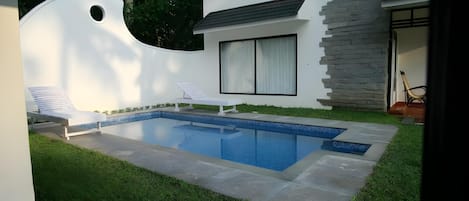 A modern house with a swimming pool, a white exterior, and a stone wall.