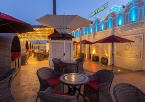 An outdoor seating area with wicker furniture and umbrellas, a building with a sign reading 'Banan Lounge,' and decorative lighting. - Banan Hotel Suite (Tabuk)