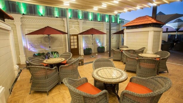 An outdoor patio with wicker furniture and umbrellas, a tiled floor, and decorative lighting. - Banan Hotel Suite (Tabuk)
