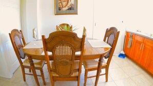 Una mesa de comedor con cuatro sillas, un cuadro en la pared y una zona de cocina con armarios.