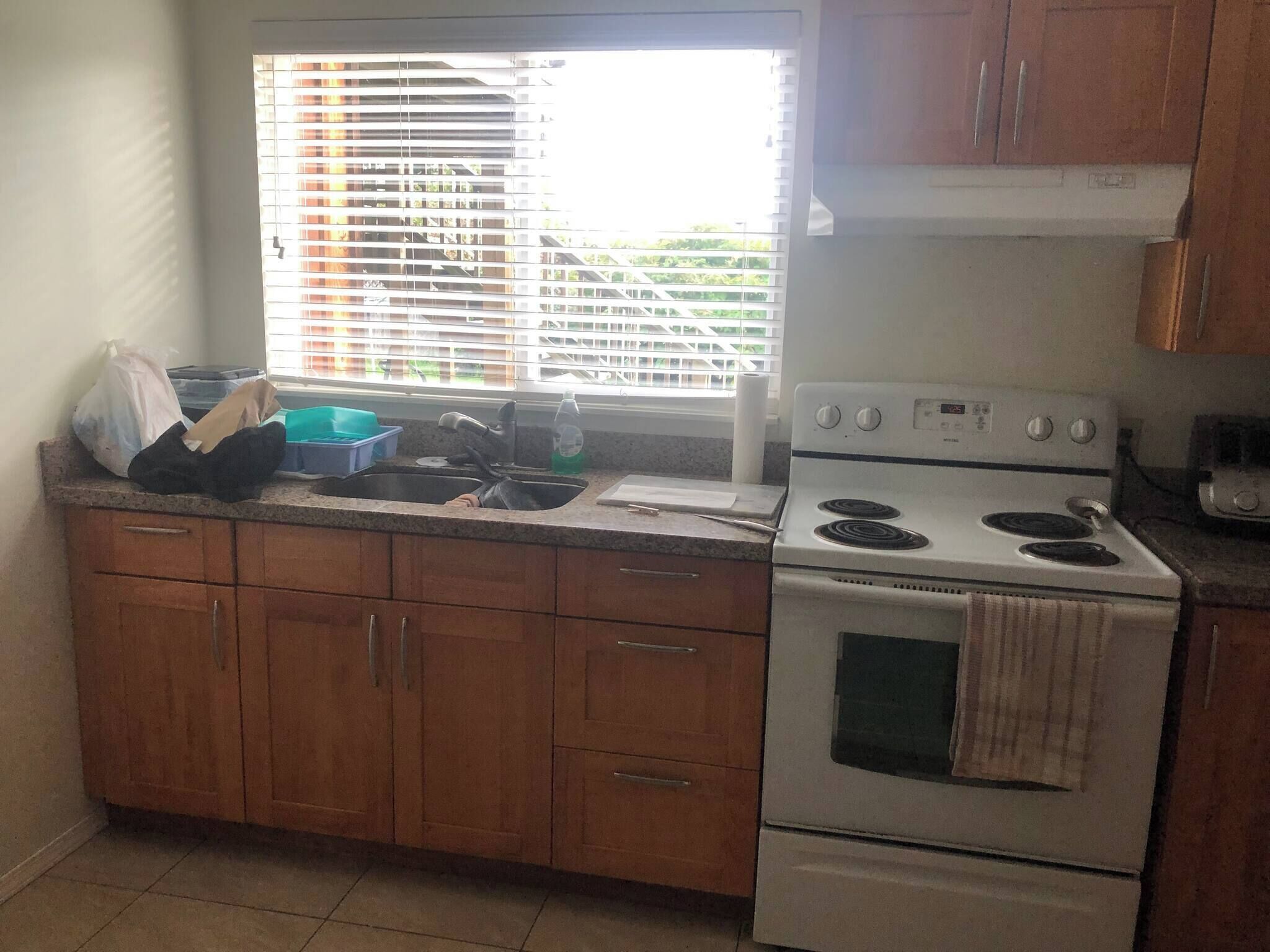 A kitchen with wooden cabinets, a white stove, and a window with blinds.