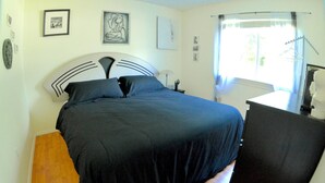Un dormitorio con cama, mesita de noche, lámpara y ventana con cortinas.