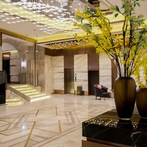 A lobby with a marble floor, a staircase, and a vase with yellow flowers.