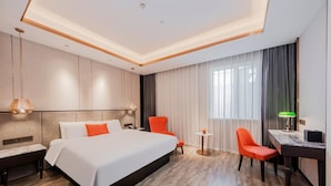 Habitación de hotel con una cama grande, un escritorio, dos sillas, una mesita y una lámpara.