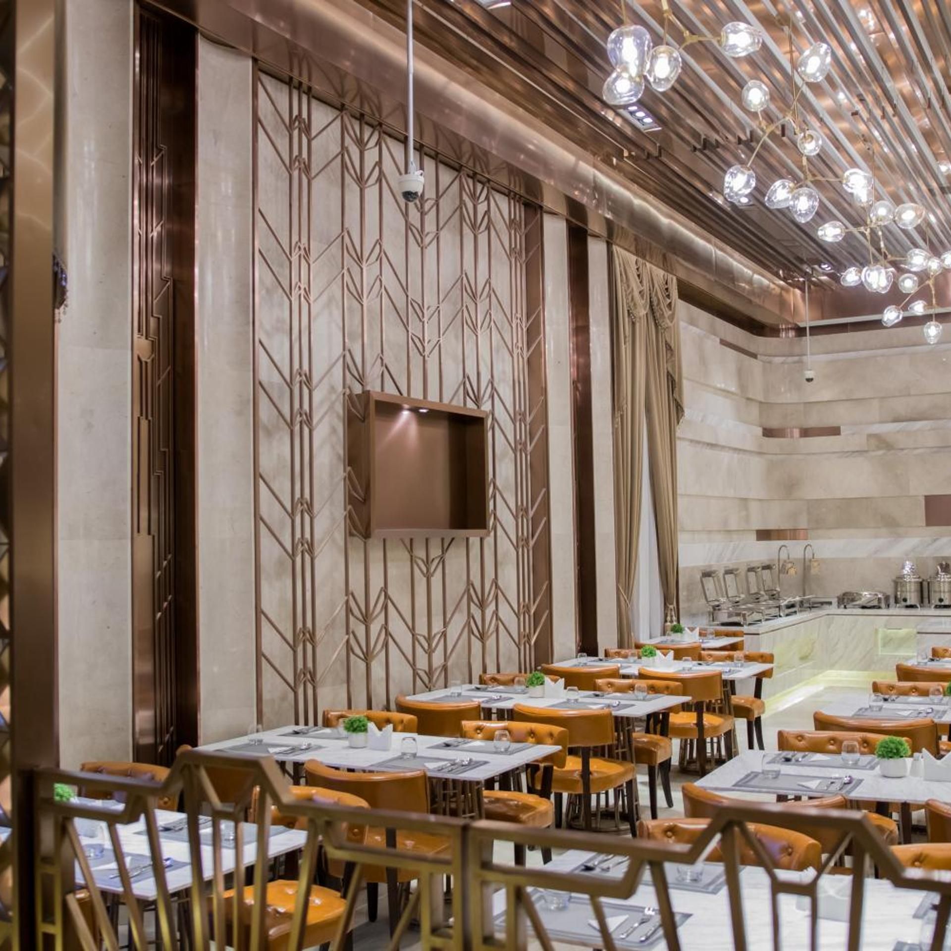 Interior de un restaurante con varias mesas y sillas, una zona de bar y una pared decorativa con diseños geométricos.