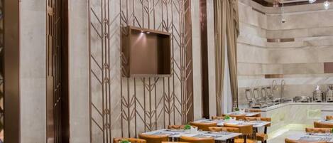 Interior de un restaurante con varias mesas y sillas, una zona de bar y una pared decorativa con diseños geométricos.