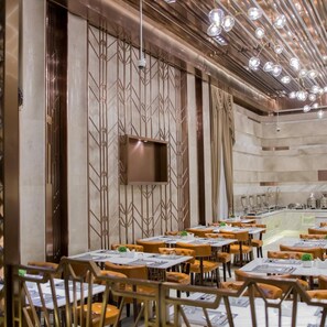 A restaurant interior with multiple tables and chairs, a bar area, and a decorative wall with geometric patterns.
