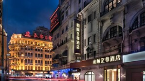 Un hotel con letreros iluminados, estilo arquitectónico clásico y vista a la calle por la noche.