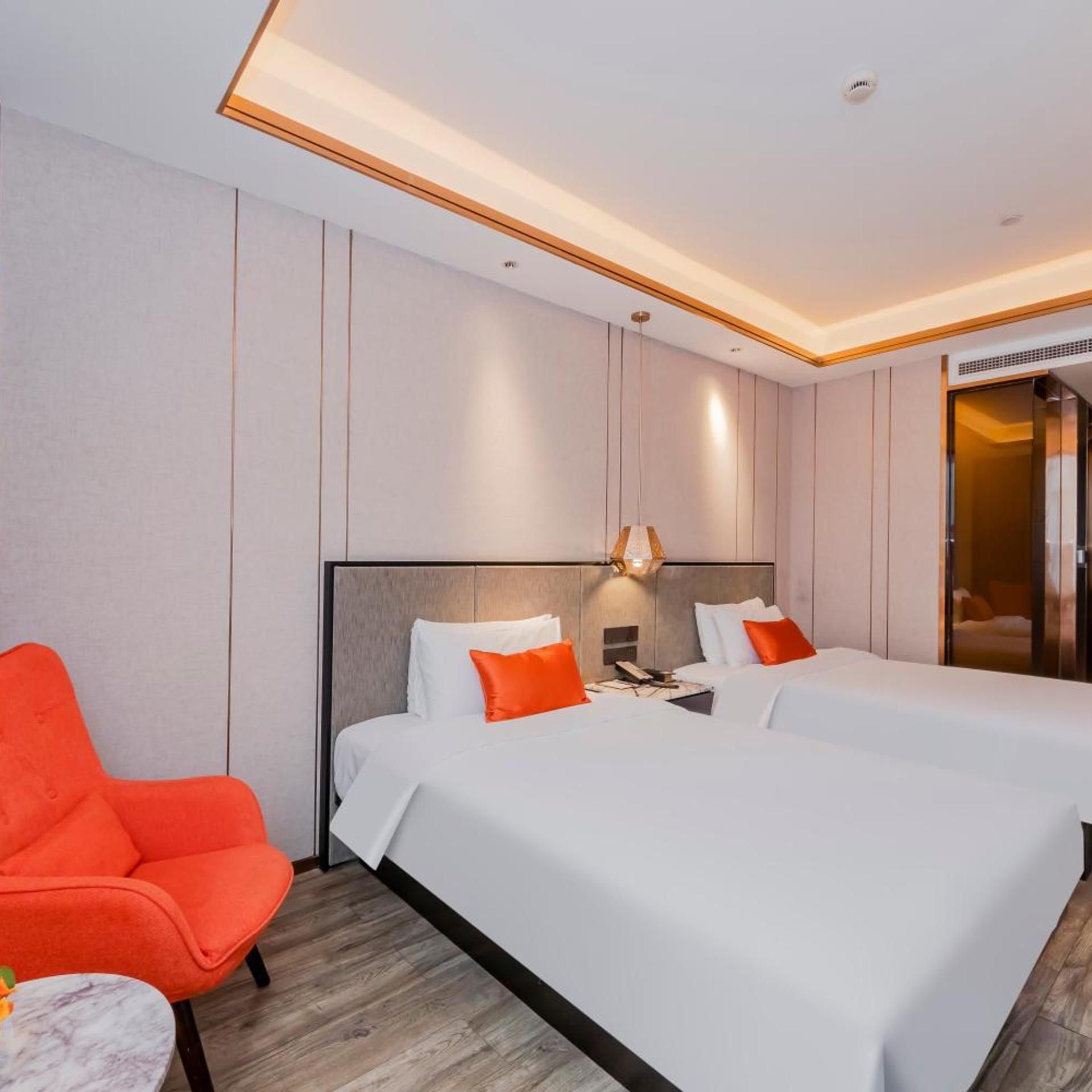 Habitación de hotel con dos camas, una silla roja, una mesita y un espejo.
