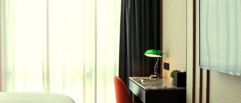 Une chambre d’hôtel avec un lit, un bureau doté d’une lampe, une chaise et une grande fenêtre avec des rideaux.