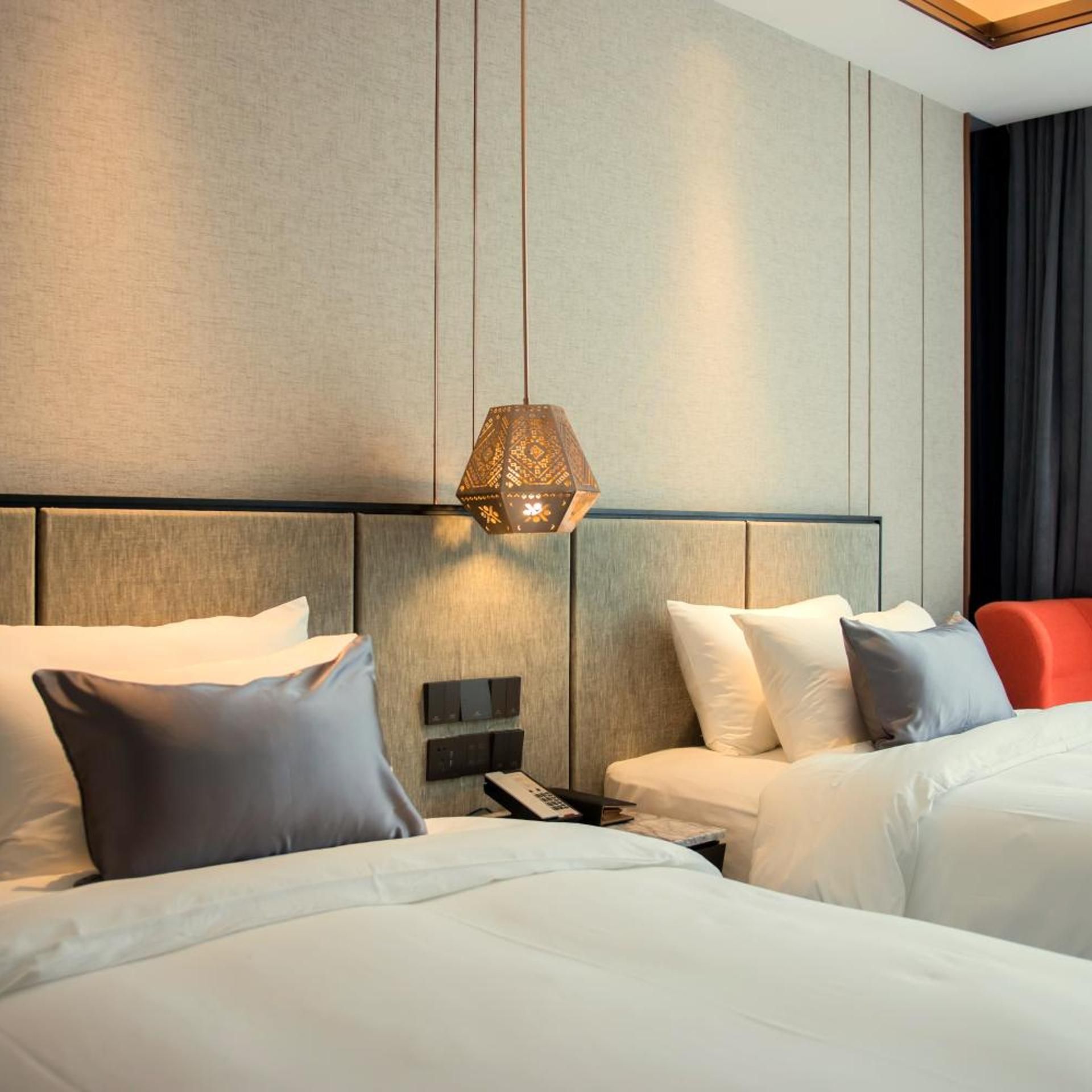 A hotel room with two beds, a modern headboard, a bedside table with a phone, and a decorative hanging light fixture.
