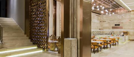 A modern hotel lobby with a staircase, a seating area, and a dining space.