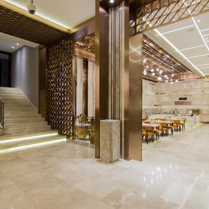 A modern hotel lobby with a staircase, a seating area, and a dining space.