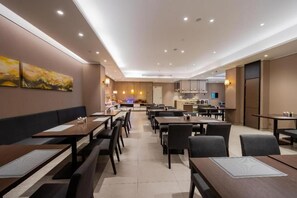 A hotel dining area with multiple tables and booths, a kitchen in the background, and artwork on the walls.